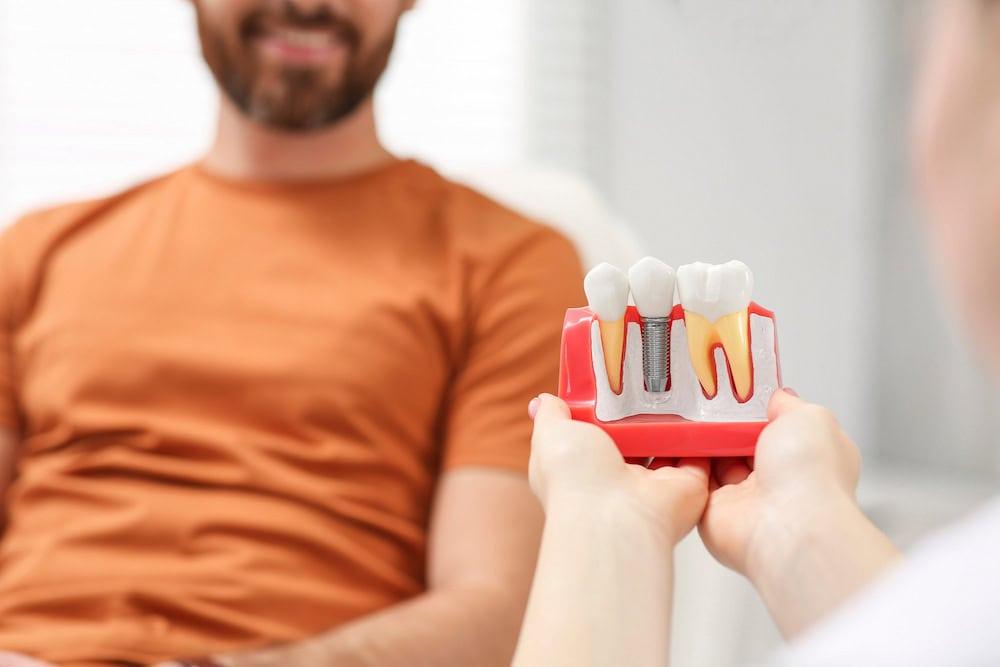 A dentist presents a mockup model of different types of dental implant materials to a patient.