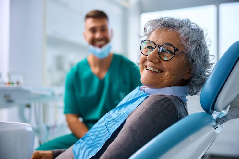 A senior woman smiles after receiving implants. Implants are generally better than dentures.