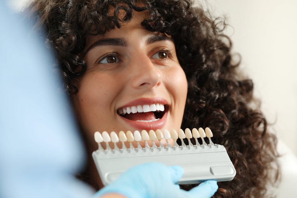 dentist examines a young woman’s teeth with veneers on. Veneers do more for looks versus braces.